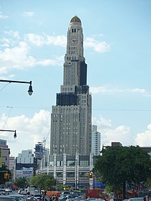 View of the Williamsburgh Savings Bank Tower from Flatbush Avenue. There is scaffolding on parts of the tower. The Atlantic Terminal shopping mall and train station is located in front of the tower.