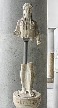 Photograph of an Ancient Greek statue of a woman, broken into two parts: a metal support holds the top and bottom together.