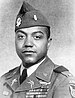 Head and shoulders of a black man with full cheeks in military uniform. Rows of ribbon bars are on his left breast and his lapels and garrison cap are adorned with pins and badges.