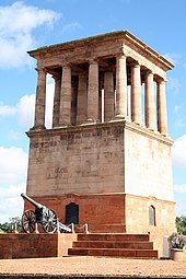 The Honoured Dead Memorial, a tall, brown sandstone building with multiple Grecian-type pillar and the Long Cecil gun at its base