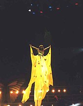 Velasquez performs in a long yellow gown while transported by wires.