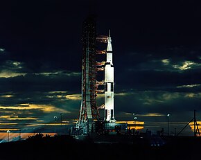 Saturn five rocket on a launch pat at dusk while cloudy outside.