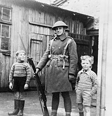 A British soldier holding a rifle with two small boys either side