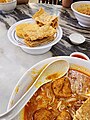 Image 46A bowl of curry mee, with fried beancurd skins and fish cake on the side (from Malaysian cuisine)