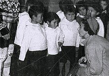 Black and white image of the Queen kneeling next to several Inuit children