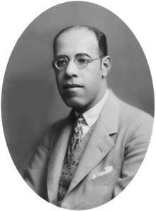 Photograph showing the head and shoulders of de Andrade with glasses wearing a suit