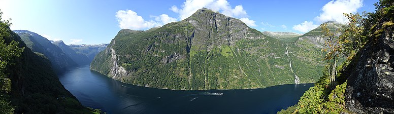 Panorama des Geirangerfjords von einer Position oberhalb von Skageflå. Das Panorama zeigt die Nordseite des Geirangerfjords in der Umgebung des Bergs Teinnosa in der Bildmitte. Links im Bild sind die Wasserfälle Die Sieben Schwestern zu sehen. Rechts neben den Sieben Schwestern befindet sich der Hof Knivsflå