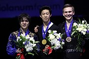 A photograph of Shoma Uno, Nathan Chen and Mikhail Kolyada (from left to right) with medals around their necks and flowers in their hands.