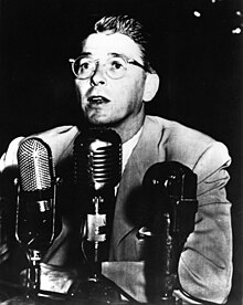 Photograph of Reagan wearing glasses and speaking in front of three microphones