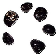 A photograph of 6 smooth black pebbles with white markings, arranged in a circle