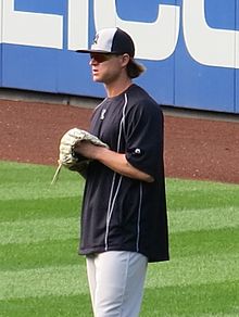 A man in a black shirt, gray baseball pants, and a black and white cap