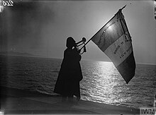 B&W photo showing a soldier blowing the trumpet while holding a flag