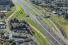 Aerial image of a wide freeway at an interchange that also includes a two-track light rail line.