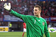 Neuer, in a Germany goalkeeper jersey and gloves, raises a hand to his right