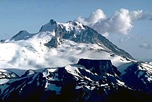 A rocky mountain with heavily glaciated lower slopes rising over a rocky ridge in the foreground.