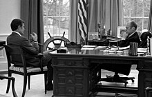 Gerald Ford sits behind the Wilson Desk talking with George H. W. Bush who sits beside it