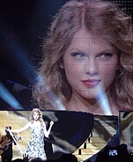 Swift striking a pose onstage as the screen behind her shows a closeup of her face