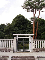 White torii and concrete fence in front of trees.