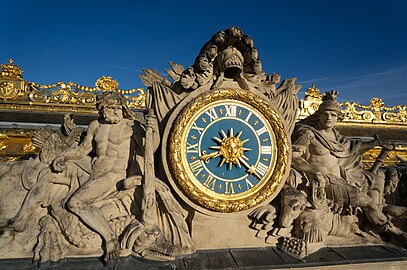 Baroque mascaron of a clock with rais, visual manifestation of the metaphor Sun King (le Roi Soleil) for Louis XIV, on the Marble Court facade of the Palace of Versailles, Versailles, France, designed by Louis Le Vau and Jules Hardouin-Mansart, c. 1660-1715