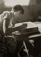 full length portrait of young woman with short hair seated working with a pencil on a litho stone