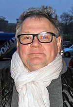 Photo of Janusz Kamiński wearing a white scarf and a black bubble vest in 2014.