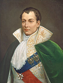 Painting of a man with a clef chin. He wears an elaborate court costume with white lace ruffle at his throat.
