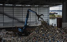 Scrap-handling crane being operated amid piles of materials after they arrive in the tipping building