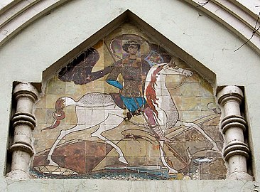 A small image of St. George, with the plot of the fresco of the Church of St. George in Staraya Ladoga in a stylized icon case on the facade, above the main porches, the maiolica was made in 1911–1913 by Anatoly Alexandrovich Ostrogradsky.
