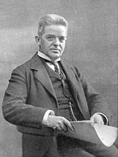 Carl Nielsen, seated, facing right, smartly dressed in a suit and waistcoat