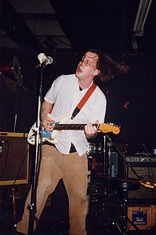 Photo of Jeff Mangum playing a guitar with a microphone nearby