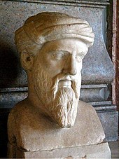 Marble bust of a man with a long, pointed beard, wearing a taenia, a kind of ancient Greek head covering in this case resembling a turban. The face is somewhat gaunt and has prominent, but thin, eyebrows, which seem halfway fixed into a scowl. The ends of his mustache are long a trail halfway down the length of his beard to about where the bottom of his chin would be if we could see it. None of the hair on his head is visible, since it is completely covered by the taenia.