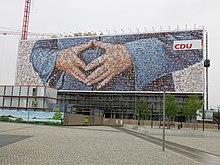 A 2013 CDU billboard near the Berlin Hauptbahnhof uses a mosaic of supporters' photographs to depict the Merkel-Raute.