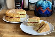 Two tier Victoria sandwich cake with a filling of strawberry jam; two slices have been taken ready to serve, and demonstrate the cake's construction