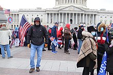 A QAnon emblem (upper left) is raised during the January 6 United States Capitol attack.