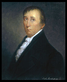 A man in his early fifties with receding black hair, wearing a ruffled white shirt and black jacket, facing left