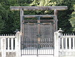 Wooden torii gate and concrete fence in front of trees.