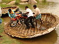 Passengers manoeuvre a motorcycle out of a woven-reed coracle ferry, near Hampi village, India. July 2008.