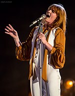 Florence Welch, in a mustard-yellow-and-white outfit, singing passionately into a microphone
