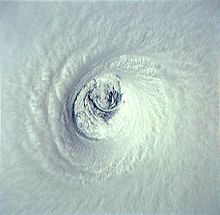 A close-up satellite image of a powerful hurricane's eye with smaller cloud swirls inside