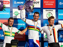Three men on a podium celebrating with their arms raised