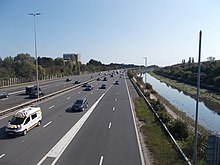 six-lane portion of highway with light traffic alongside a narrow waterway under a blue sky