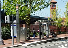 The platform of Union Station/Northwest 5th & Glisan station with riders waiting near the shelter and the Portland Union Station clock tower in the background