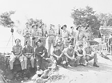 A black and white informal photograph of a group of men in various uniforms,; some are seated, some are standing