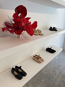 Two white shelves of shoes, with a vase of red flowers