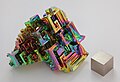 A bismuth crystal with a thin iridescent layer of bismuth oxide, with a whitish-silver bismuth cube for comparison