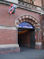 A brick and stone arched entrance with the London Underground roundel sign fixed to the wall alongside.