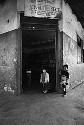 A black and white photo of two children in front of a store with a sign that says: "NON-WHITE SHOP This notice is displayed in accordance with the provisions of the Shop Hours Ordinance. 1959."