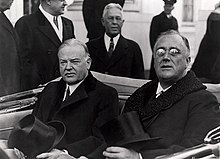 Hoover and Roosevelt sit in the back seat of an open top car with their hats on their laps.