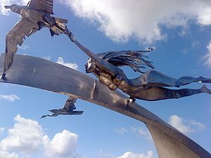 Shiny steel sculpture of woman gliding over a wave along with two seagulls