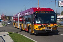 A red-and-yellow articulated bus seen on a suburban street from a nearby sidewalk. The bus's front sign reads "[A] Federal Way TC".